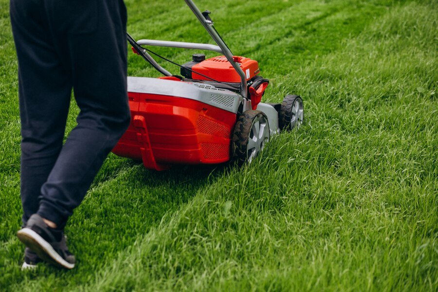 Person mowing a green lawn with a red and gray lawnmower.